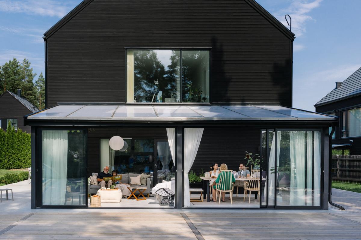 Bild på ett uterum Fira från Skånska Byggvaror, fasadmonterat på ett svart hus. En familj sitter i uterummet.